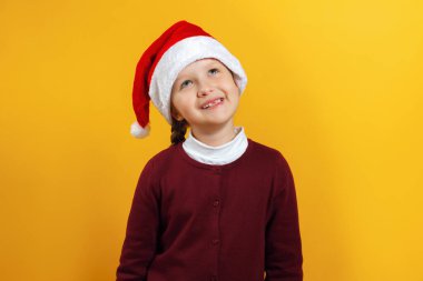 Noel Baba şapkalı mutlu küçük bir kızın büyüleyici portresi. Çocuk rüyasında sarı bir arka plana bakıyor.