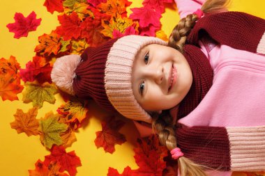 Sonbahar yapraklarının üzerinde yatan mutlu küçük kız. Atkı ve şapkalı bir çocuk. Üst görünüm