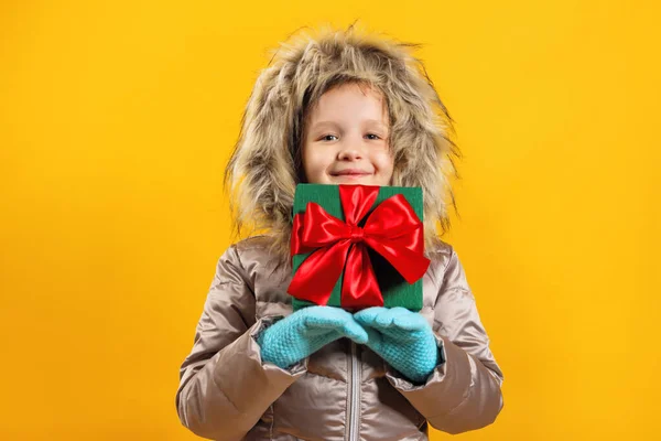 Il bambino tiene una scatola con un regalo in mano. Ritratto di una bambina carina felice con un piumino su uno sfondo giallo — Foto Stock