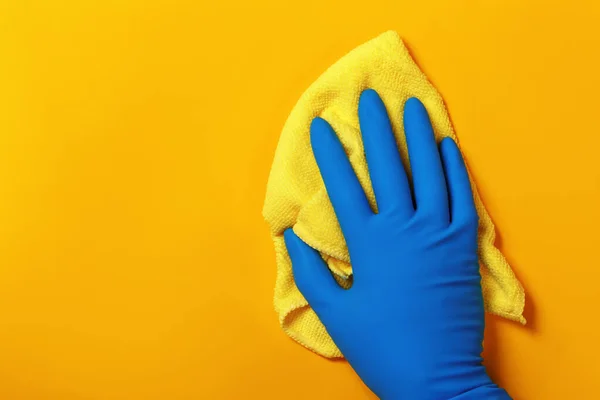 Una mano in un guanto di lattice protettivo tiene uno straccio su uno sfondo giallo — Foto Stock