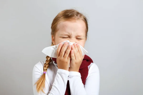 Ein kleines Mädchen in einem warmen Schal pustet ihr auf die Nase. krankes Kind auf grauem Hintergrund. kalte Jahreszeit — Stockfoto