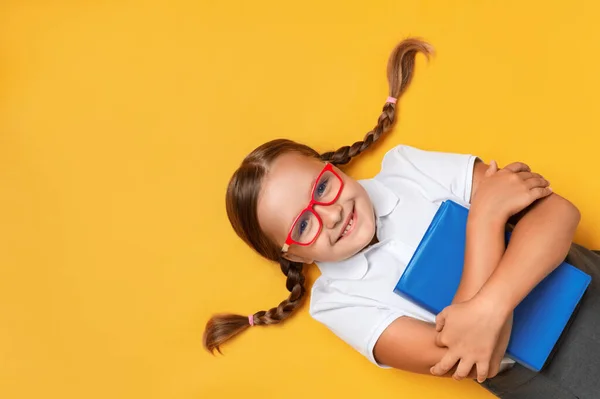 可爱的小女孩戴着眼镜 带着一本黄色背景的书 顶部视图 — 图库照片