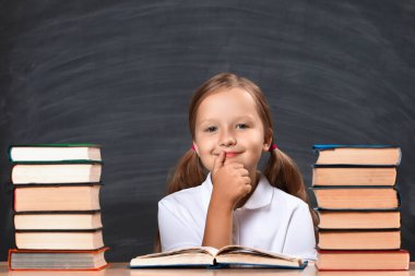 Okulun arka planında, masada oturan küçük kız öğrenci kara kara tahtası. Kitap yığınları arasında düşünceli bir çocuk. Eğitim kavramı.