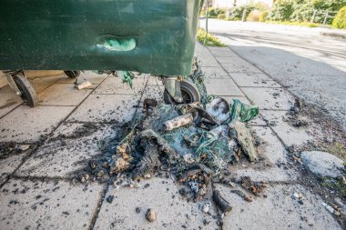 Plastik bir çöp tenekesi yanmış ve erimiş kalıntılar yerde..