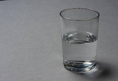 Gri zemin üzerinde yarım bardak boş su.