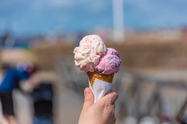 Pink and white ice cream in a cone melting in the sun