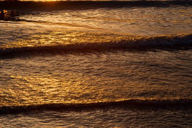 Küçük bir kumsalda, altın bir günbatımında dalgalar