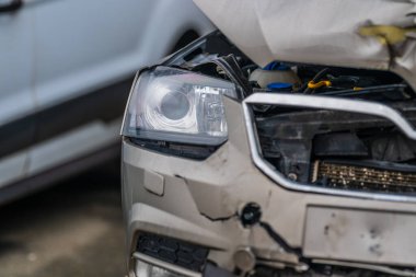 Otoparkta hasar görmüş gümüş araba ön tarafta çarpışma var.