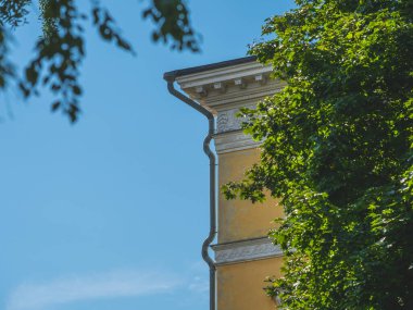 Ağaçlarla çevrili dekoratif çatılı bir bina köşesi.