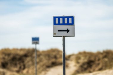 Kumlu yol arka planında yön oklu park işareti