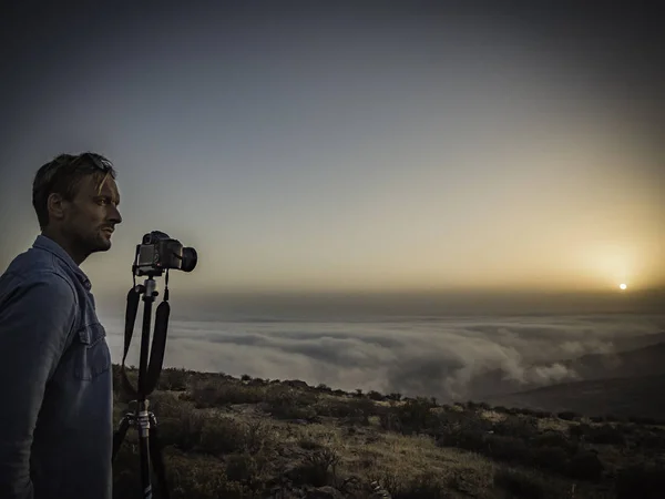 Bir dağın tepesinde bulutların üzerinde güzel bir gün batımının fotoğrafını çeken adam