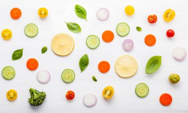 Ham salata, marul yaprağı, salatalık, domates, havuç, brokoli, fesleğen, soğan ve limon içeren besin örnekleri beyaz ahşap zemin üzerinde yatıyordu..