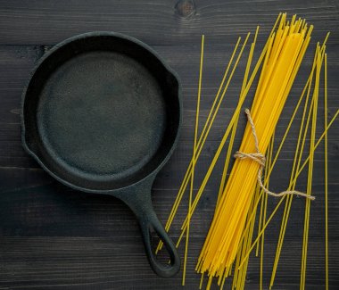 Siyah ahşap arka plandaki ince spagetti. Kopya alanı olan sarı İtalyan makarnası. İtalyan yemeği ve menü konsepti.