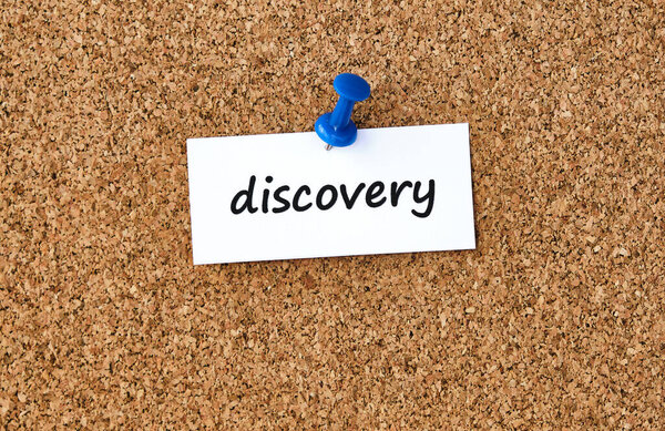 Discovery. Word written on a piece of paper or note, cork board background.