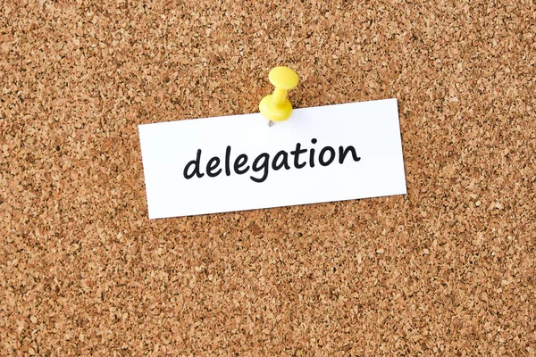 Delegation. Word written on a piece of paper or note, cork board background.