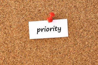 Öncelik. Bir parça kağıda veya nota yazılmış sözcük, mantar tahtası arka planı.