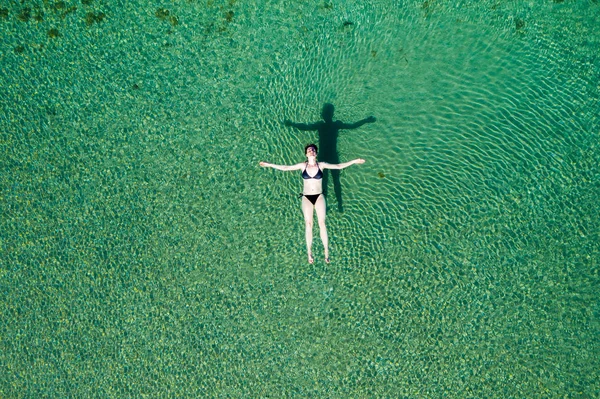 Woman in bikini floating on back on the surface of crystal clear water, young woman carefree on the sea, relaxing, Dugi otok island, Croatia, overhead drone view