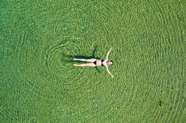 Woman in bikini floating on back on the surface of crystal clear water, young woman carefree on the sea, relaxing, Dugi otok island, Croatia, overhead drone view