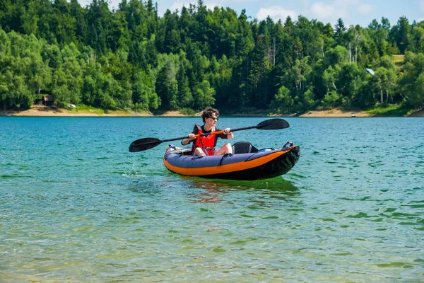 Young active woman kayaking in inflatable kayak on lake Lokve, in Gorski kotar, Croatia. Adventurous experience on a beautiful sunny day.