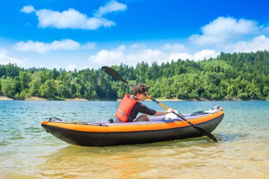 Hırvatistan'ın Gorski kotar kentinde, Lokve Gölü'nde şişme kayıkta kürek çeken kadın. Vahşi doğada maceracı deneyim.