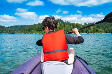 Hırvatistan'ın Gorski kotar kentinde, Lokve Gölü'nde şişme kayıkta kürek çeken kadın. Vahşi doğada maceracı deneyim.