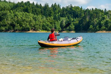 Hırvatistan'ın Gorski kotar kentinde, Lokve Gölü'nde şişme kayıkta kürek çeken kadın. Vahşi doğada maceracı deneyim.