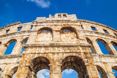 Monumental ancient Roman arena in Pula, Istria, Croatia, historic amphitheater wide angle view of high walls on blue sky background