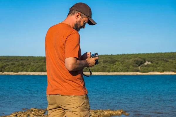 Photographer man in t-shirt and cargo pants walking around sea shore with camera and shooting nature, half body portrait, landscape photography concept