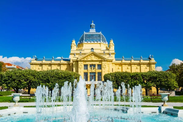 Zagreb, Hırvatistan 'ın başkenti. Klasik 19. yüzyıl mimarisi, güneşli bir günde şehir merkezindeki parkta sanat pavyonu ve ön planda çiçekler..