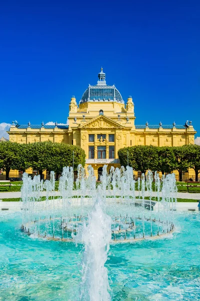 Zagreb, Hırvatistan 'ın başkenti. Klasik 19. yüzyıl mimarisi, güneşli bir günde şehir merkezindeki parkta sanat pavyonu ve ön planda çiçekler..