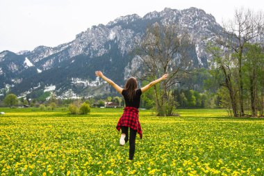 Sarı çiçekler karahindiba ve dağlar, Bavyera, Fussen güzel Bavyera alanı üzerinde üst ellerini yükselterek genç kadının geri görünümü. Seyahat konsepti. 