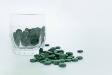 Spirulina tabletler beyaz arka plan üzerinde bir cam