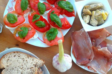 tablo ile atıştırmalıklar, mozzarella domates, enginar, soğuk füme et, sarımsak, ekmek ve yaprakları, fesleğen