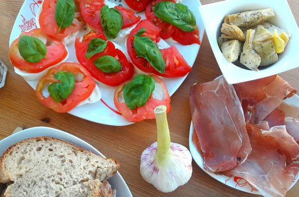 tablo ile atıştırmalıklar, mozzarella domates, enginar, soğuk füme et, sarımsak, ekmek ve yaprakları, fesleğen