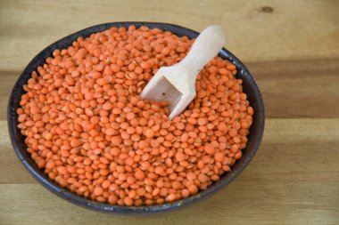 siyah bir kapta haşlanmış kırmızı mercimek ve tahta bir kaşık la tahta bir tahta üzerine dağınık