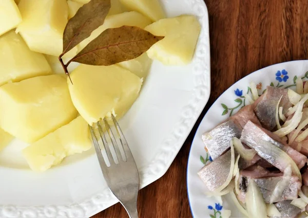 Herring fillet with onions, boiled potatoes, bay foxes and mini tomatoes on a white plate