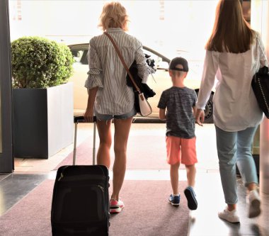 bir bavul ve bir erkek ile iki kız taksi için otelden çıkıyor