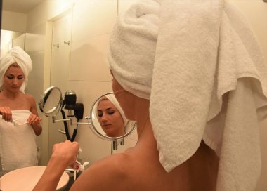 ayna yakınında diş fırçası ve beyaz havlu ile banyoda genç kadın