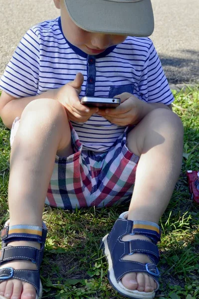 Ragazzo Pantaloncini Siede Sull Erba Con Uno Smartphone Mano — Foto Stock