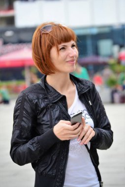 Elinde akıllı bir telefonla siyah ceketli bir kız.