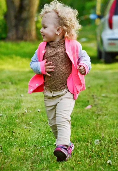 穿着粉色毛衣的卷曲金发姑娘走在绿草上 — 图库照片