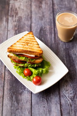 Ahşap arka plan üzerinde peynir, domates, salatalık, sosis ve salata ile Sandviç. Sütlü kahve. Dikey yönlendirme