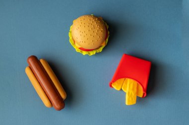Plastik burger, salata, domates, mavi arka planda sosisli patates kızartma. Yatay yönlendirme. Çocuk oyuncakları. Zararlı yapay gıda kavramı. Plastik organik değil. Sağlıklı değil.