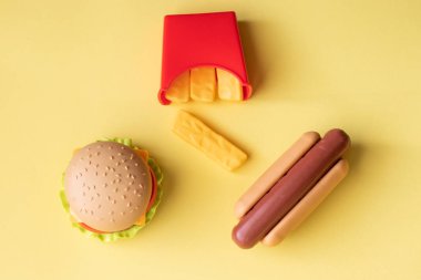 Plastik burger, salata, domates, sarı arka planda sosisli patates kızartma. Yatay yönlendirme. Çocuk oyuncakları. Zararlı yapay gıda kavramı. Plastik organik değil. Sağlıklı değil.