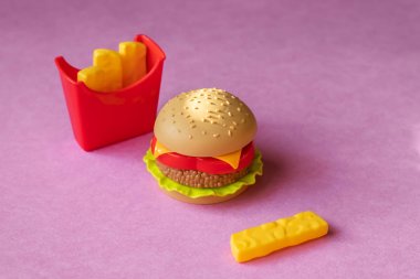 Plastik burger, salata, domates, pembe arka planda patates kızartması. Yatay yönlendirme. Çocuk oyuncakları. Zararlı yapay gıda kavramı. Plastik organik değil. Sağlıklı değil.
