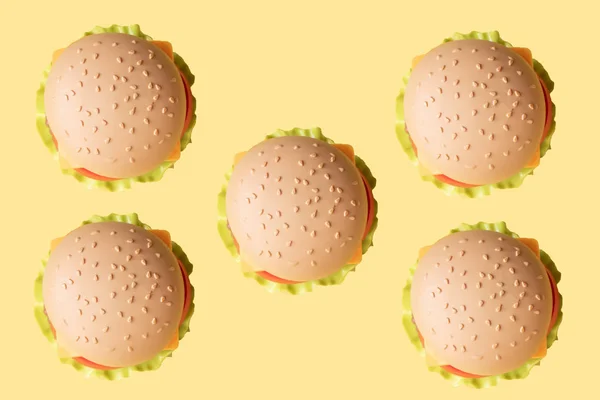 Hamburger di plastica, insalata, pomodoro, su fondo giallo. Orientamento verticale. Giocattolo per bambini. Il concetto di cibo artificiale dannoso. Plastica Non organica. Non sano . — Foto Stock