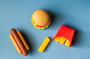 Plastik burger, salata, domates, mavi arka planda sosisli patates kızartma. Yatay yönlendirme. Çocuk oyuncakları. Zararlı yapay gıda kavramı. Plastik organik değil. Sağlıklı değil.