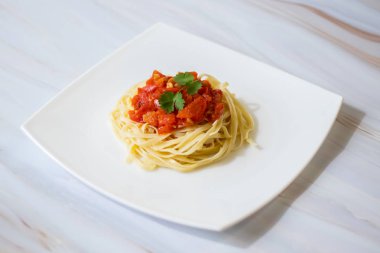 Taze domates ile Makarna, hafif bir arka plan ve beyaz bir kare plaka üzerinde zeytinyağı ve sarımsak ile pişirilir. İtalyan yemeği. Yatay yönlendirme