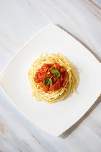 Pasta with fresh tomatoes, cooked with olive oil and garlic on a light background and a white square plate. Italian food. Vertical orientation