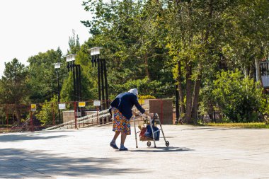 Yaşlılık neşe değildir. Çantalı yaşlı bir kadının yan görüntüsü. Yalnız yaşlı kadın.